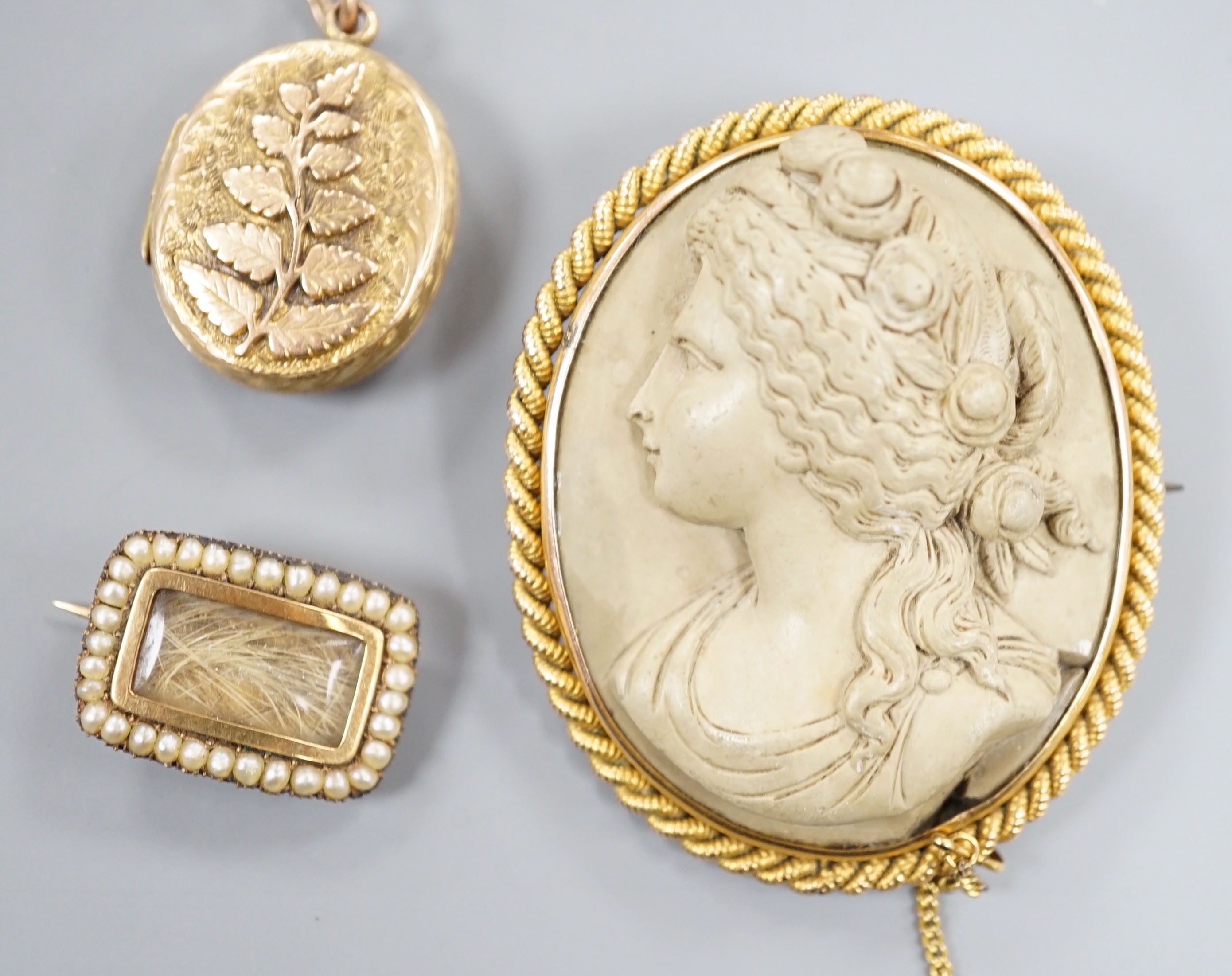 A 19th century yellow metal, seed pearl and plaited hair set mourning brooch, 20mm, a yellow metal oval locket and a mounted lava brooch.